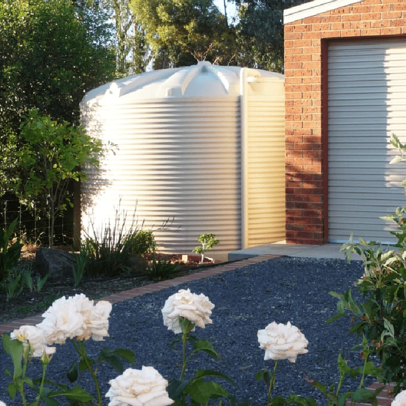 Polymaster 22500L Round Rainwater Tank In White next to a house